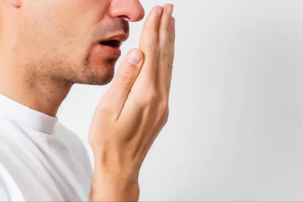 Man breathing onto his hand to smell his breath